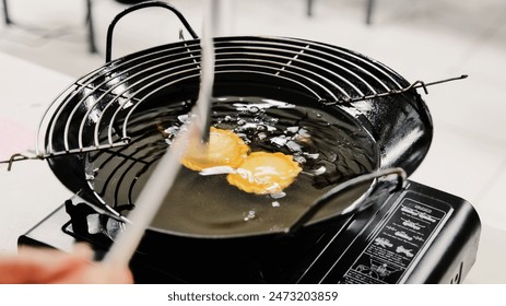 Curry puff cake is in the process of being fried in a black frying pan and portable stove.