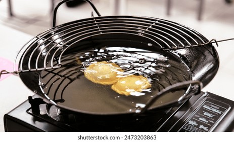Curry puff cake is in the process of being fried in a black frying pan and portable stove.