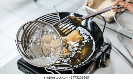 Curry puff cake is in the process of being fried in a black frying pan and portable stove.