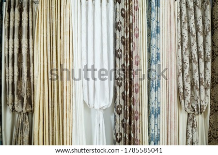 Curtain samples hanging from hangers on rail in store. Fabric texture samples selection fabrics for interior decoration Curtains, tulle and furniture upholstery.