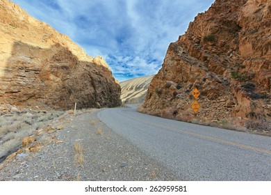 Curve on Death Valley road between red rocks with road sign - Powered by Shutterstock