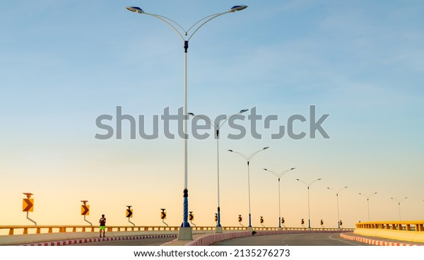 Curve road with street lamp pole and yellow curve\
traffic sign. Back view of a man running on footpath beside empty\
road. Red-white prohibited stop sign. Solar panel energy on curve\
traffic sign.