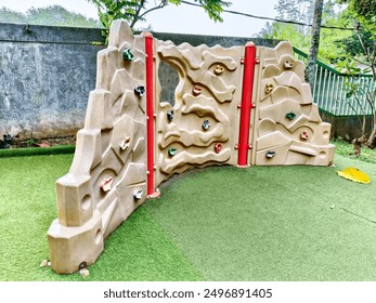 a curved climbing wall in a playground. The wall is made of a beige, textured material with red handholds and foot pegs. - Powered by Shutterstock