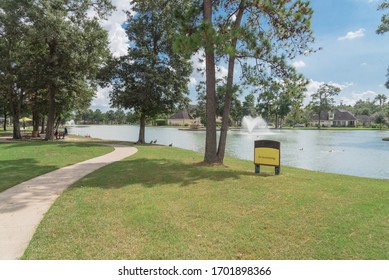 Curved Concrete Pathway At Suburban Park In Houston, Texas, USA. Matured Trees With Duck Swimming, A Little Duck House And Lakeside Mansion In Distance, People Relax On Picnic Bench. No Swimming Sign