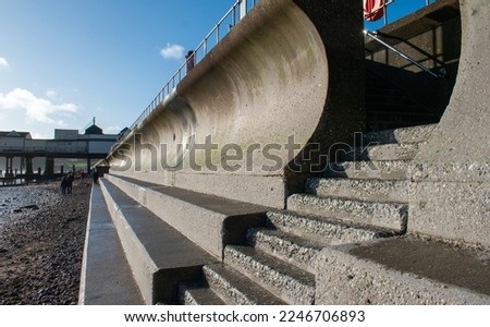 Curved concrete sea wall with concrete steps in foreground. Civil engineering and flood prevention through reinforced coastal sea defenses.