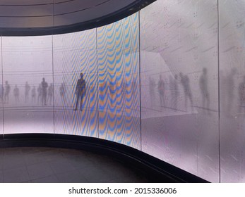 A curved led digital display screen wall. The wall is depicting moving shadows of people on a white background. 