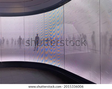 A curved led digital display screen wall. The wall is depicting moving shadows of people on a white background. 