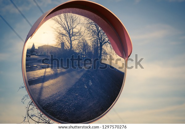 A curved mirror on the road. The mirror reflects\
the roads, the trees and the setting sun. In the background is the\
blue sky. Retro colors.