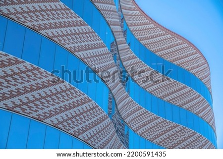 Curved modern building with bricks and reflective glass walls at downtown Tucson, Arizona. Low angle view of a modern building exterior against the blue sky background.
