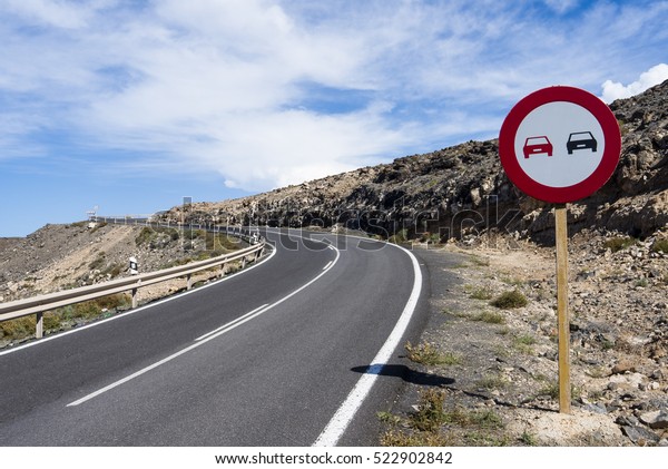 Curved mountain road at blue skies with a road\
sign reading do not\
overtake.