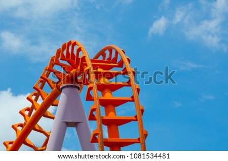 Curved of orange Roller Coaster track in close up isolated on blue sky background.