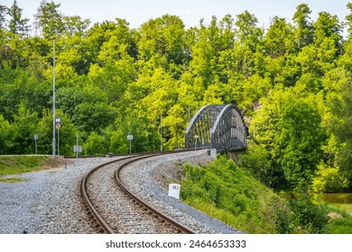 A curved railway bridge in Rataje surrounded by dense greenery and trees during summer, with railway tracks leading up to the bridge. - Powered by Shutterstock