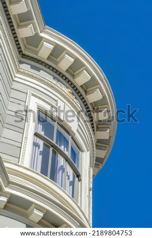 Curved window wall of a victorian style building in San Francisco, California. Low angle view of a building with gray concrete lined wall and decorative frieze board and dentils.