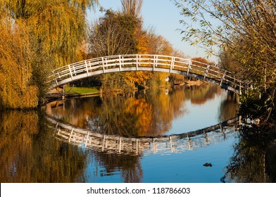 Curved wooden bridge over a small canal in a Dutch autumn landscape.