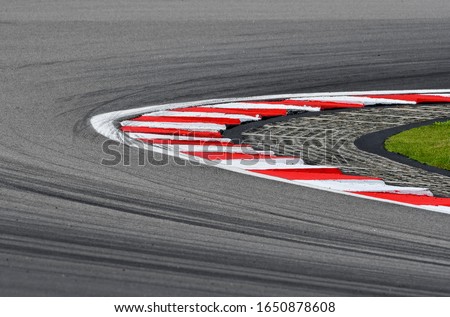 Curving asphalt red and white kerb of a race track detail. Motorsports racing circuit close up with tire mark.