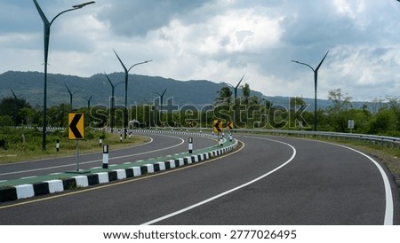 Curving empty highway with chevron direction signs and green mountain landscape.