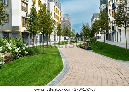 A curving paved path through the green lawn and young trees of a well-landscaped courtyard in a modern residential apartment block complex