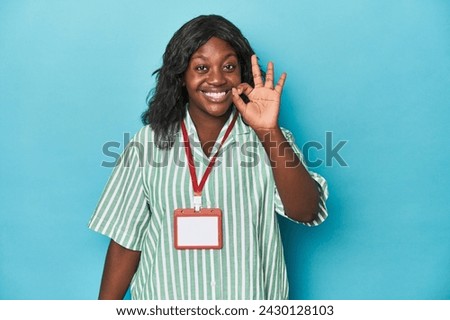 Curvy cashier with ID at supermarket cheerful and confident showing ok gesture.