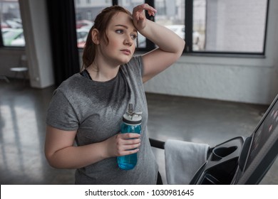 Curvy girl with water bottle on treadmill in gym