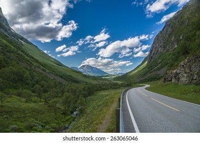 Curvy and lonely road between norwegian mountains under blue sky