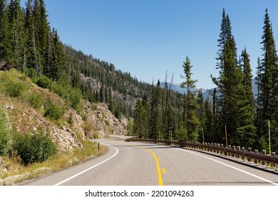 Curvy S Curve Road Adventure Path Through Forest, Mountains And Rocky Hills On A Clear Sunny Morning In Yellowstone National Park Wyoming Near The East Entrance