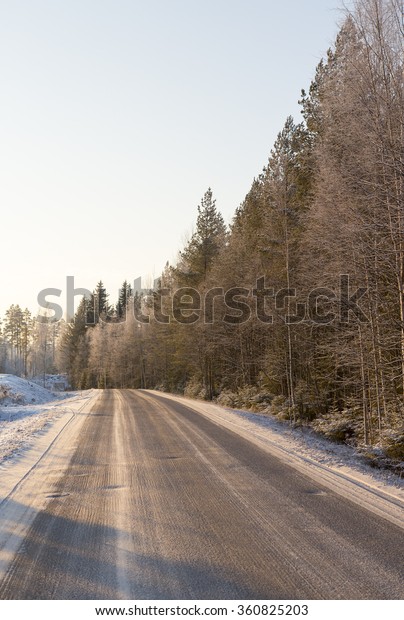 A curvy and snowy road\
in the morning. Sun is about to rise and lightens up a bit of the\
forest.