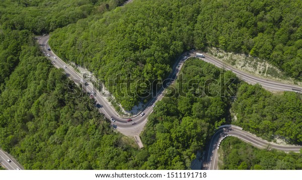 Curvy windy road between green mountain\
forest, top down aerial view. Summer\
landscape.