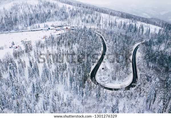 Curvy windy road in snow covered forest, top\
down aerial view. Winter landscape.\

