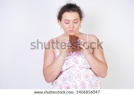 curvy woman in funny pajamas with a chocolate bar stands on a white background in the Studio