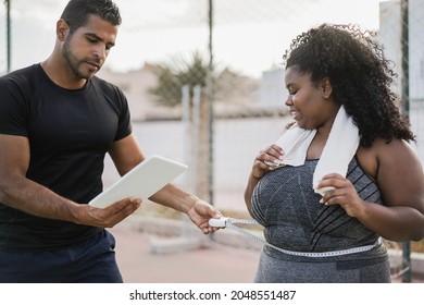 Curvy Woman With Her Personal Trainer Measuring Body Waist Outdoor - Focus On African Girl Face