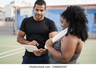 Curvy woman talking with her personal trainer while checking tech clipboard outdoor - Sport and plus size people concept - Focus on man coach face - Powered by Shutterstock