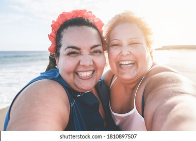 Curvy women friends taking selfie on the beach with sunset in background - Soft focus on right female face