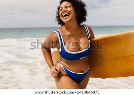 Curvy young woman enjoys beach activities, celebrating summer on a solo vacation. Female surfer carrying a board and wearing a bikini, capturing the essence of a fun and authentic summer holiday.