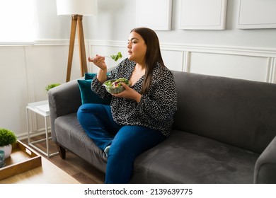 Curvy Young Woman Sitting On The Sofa And Eating A Green Salad. Fat Woman Following A Healthy Diet To Lose Weight