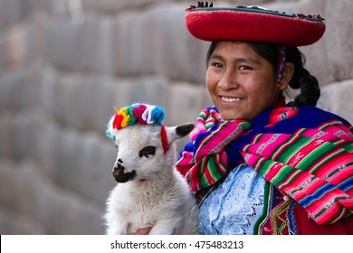 Cusco, Peru - May 14 : Jenni, a young woman dressed in colorful traditional native Peruvian closing holding a baby Lamb with Inca walls in the background. May 14 2016, Cusco Peru.