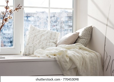 cushions and a knitted plaid on the windowsill. A cozy winter window sill. 