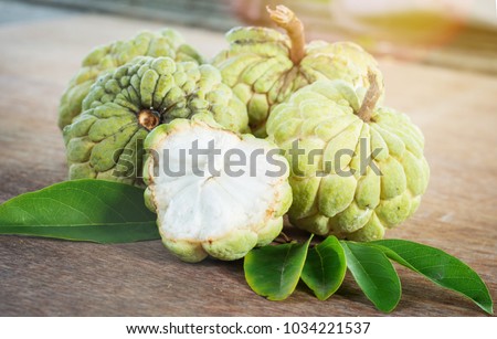 Custard apple tropical fruit showing the green skin and white flesh look delicious on with green leaf a wooden background, (Sugar Apple, Annona, sweetsop). Thai fruit.