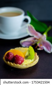 A Custard Tart With The Fruits  Such As Raspberry, Kiwi, Mango Served On A Black Slate , Coffee Cup And Lily Flower On The Black Background. 