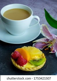 A Custard Tart With The Fruits  Such As Raspberry, Kiwi, Mango Served On A Black Slate , Coffee Cup And Lily Flower On The Black Background. 