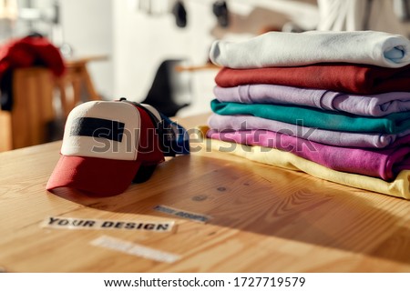 Custom apparel, clothes neatly folded on shelves. Stack of colorful clothing and baseball cap in the store. Horizontal shot. Selective focus