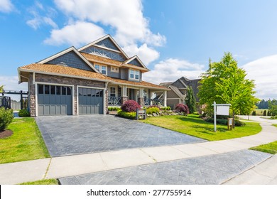 Custom built luxury house for sale with nicely trimmed and designed front yard, lawn in a residential neighborhood in Canada. For sale sign in front of the house by real estate agency. 