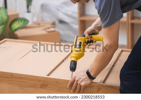 Custom furniture assembling handyman fixing fasteners on wooden cabinet back side with professional screwdriver quality carpentry services specialist working with wood materials