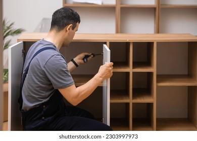 Custom furniture delivery and assembly master attaching white door to wooden cabinet in house of customer specialist in uniform working with wood in room carpentry industry