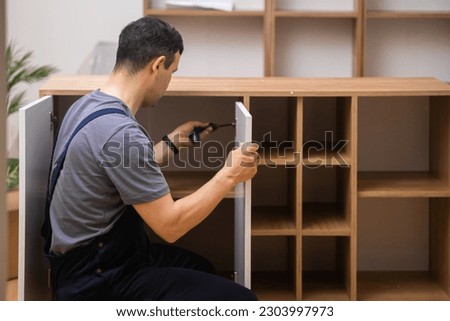 Custom furniture delivery and assembly master attaching white door to wooden cabinet in house of customer specialist in uniform working with wood in room carpentry industry