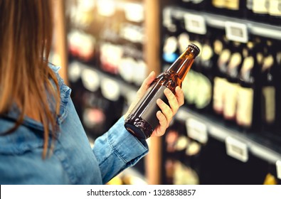 Customer Buying Beer In Liquor Store. Lager, Craft Or Wheat Beer. IPA Or Pale Ale. Woman At Alcohol Shelf. Drink Section And Aisle In Supermarket. Lady Holding Bottle In Hand. Drink Business Concept.