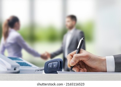 Customer And Car Salesman Shaking Hands At The Car Dealership, Businessman Signing A Contract In The Foreground