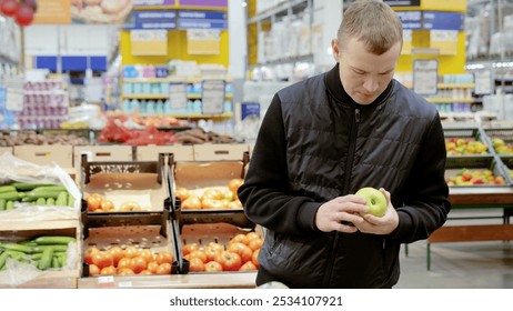 Customer carefully choosing a green apple in a grocery store produce section with vibrant fruits and vegetables in the background. Blurred shelves add freshness and variety - Powered by Shutterstock