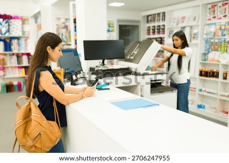 Customer checking phone at counter while employee is operating a copier machine in a modern copy and print store