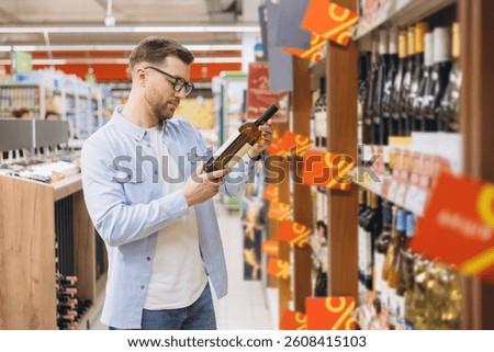 Customer checking wine bottle label during grocery shopping in supermarket alcohol section