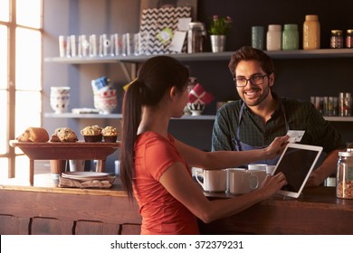 Customer In Coffee Shop Paying Using Digital Tablet Reader